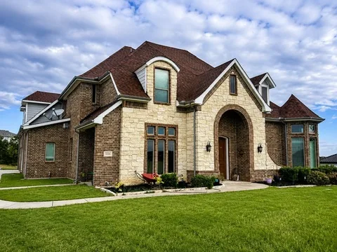 A brick and stone home in daylight with clean, uncluttered rooflines over a green lawn