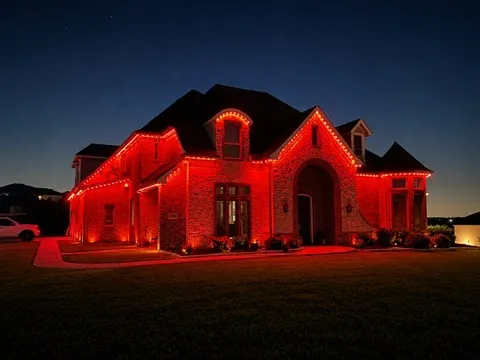 The same home lit entirely in red, roofline to landscape uplights