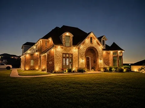Brick and stone home at dusk under a deep blue sky, warm white permanent lighting tracing every roofline