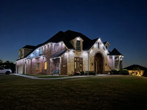 The same home after full dark in warm white, with the driveway and garage in frame